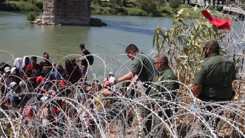 Shocking moment crowd of 100 migrants storm across Rio Grande, leaving Border Control guards with no choice but to cut razor wire and let them into Eagle Pass after four-hour stand-off in searing 101-degree heat