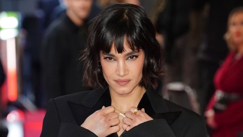Sofia Boutella shows off her toned midriff in a cropped black satin blazer and low-rise trousers as...
