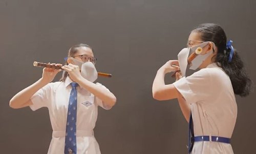Pro-China authorities in Hong Kong are mocked for forcing children to wear cumbersome double Covid masks while playing the FLUTE in propaganda video