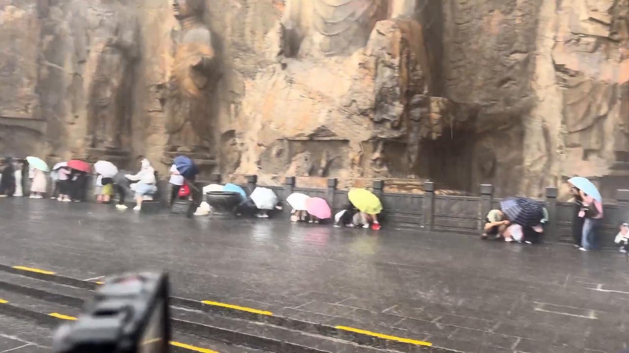 China: Tourists shelter under buddha statues as torrential rain hits Longmen Grottoes in China.