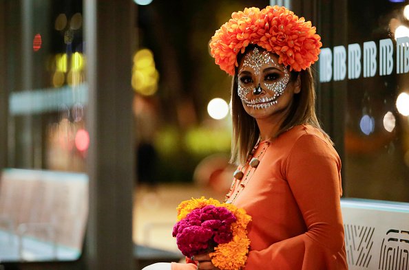 A woman wears a orange dress and painted as skull, poses for photos...