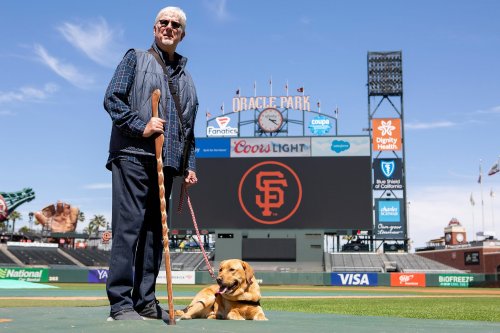 Giants announcer Mike Krukow leans on his service dog, Patriot, for support