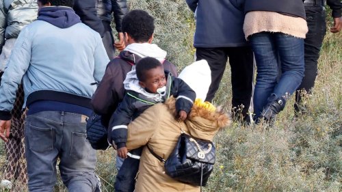 Moment crying tot sucking dummy carried across sand dunes in France as 200 migrants try to cross Channel