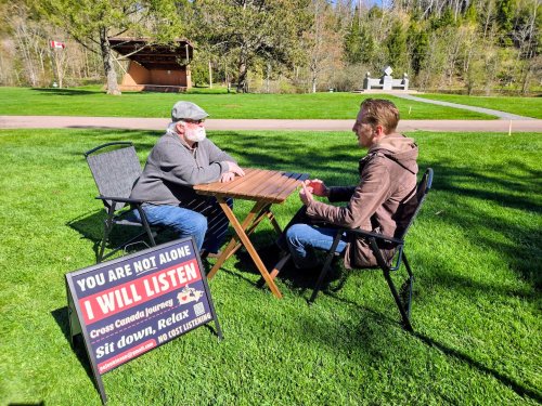 Man sits with chairs and his sign: ‘You are not alone. I will listen.’